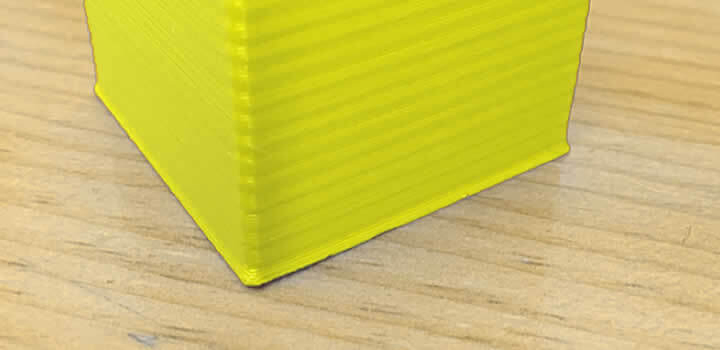 Bordas da impressão saindo da peça ou pata de elefante com filamento 3d pla amarelo impresso em cima de mesa de madeira