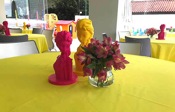 Foto de uma festa de criança focando uma mesa com toalha amarela e peças 3d impressas em filamento 3d amarelo e rosa dos personagens frozen