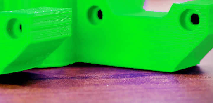 foto de parte de uma peça verde impressa com filamento abs verde-limão para impressora 3d soltando da mesa da impressora 3d em uma mesa de madeira